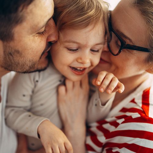 Parents either side of child's face kissing them